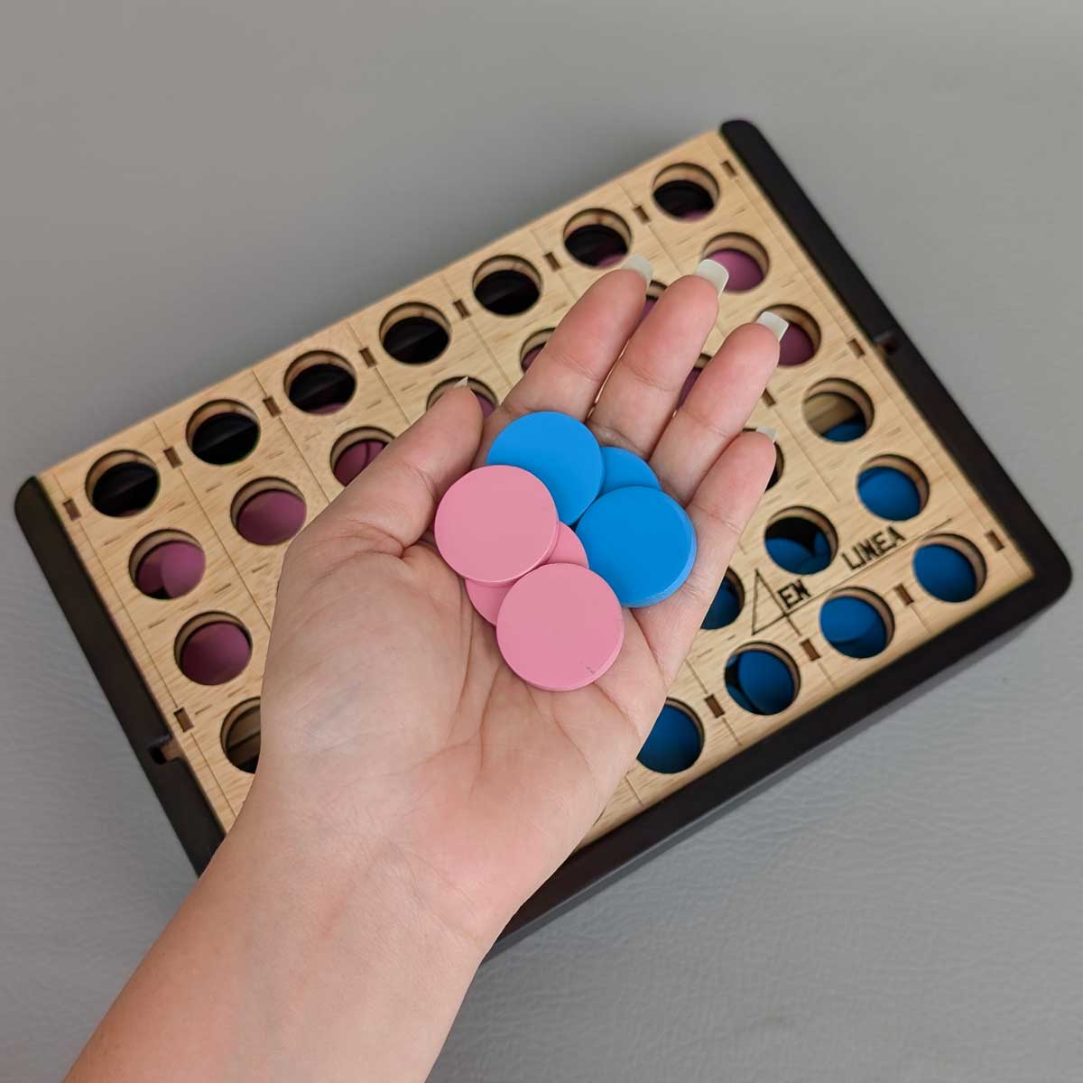 Juego 4 en línea de madera, perfecto para jugar en familia y estimular el pensamiento lógico. Foto detalle fichas, referencia tamaño en mano