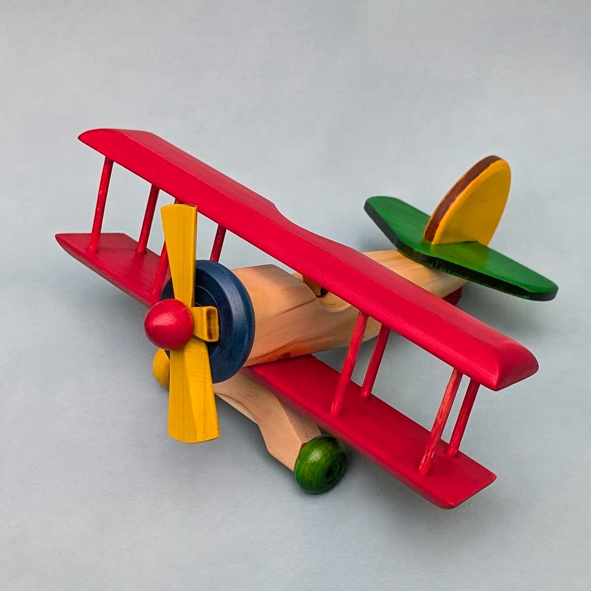 Avión biplano de madera multicolor, juguete artesanal para niños que estimula la imaginación. Color de alas rojo