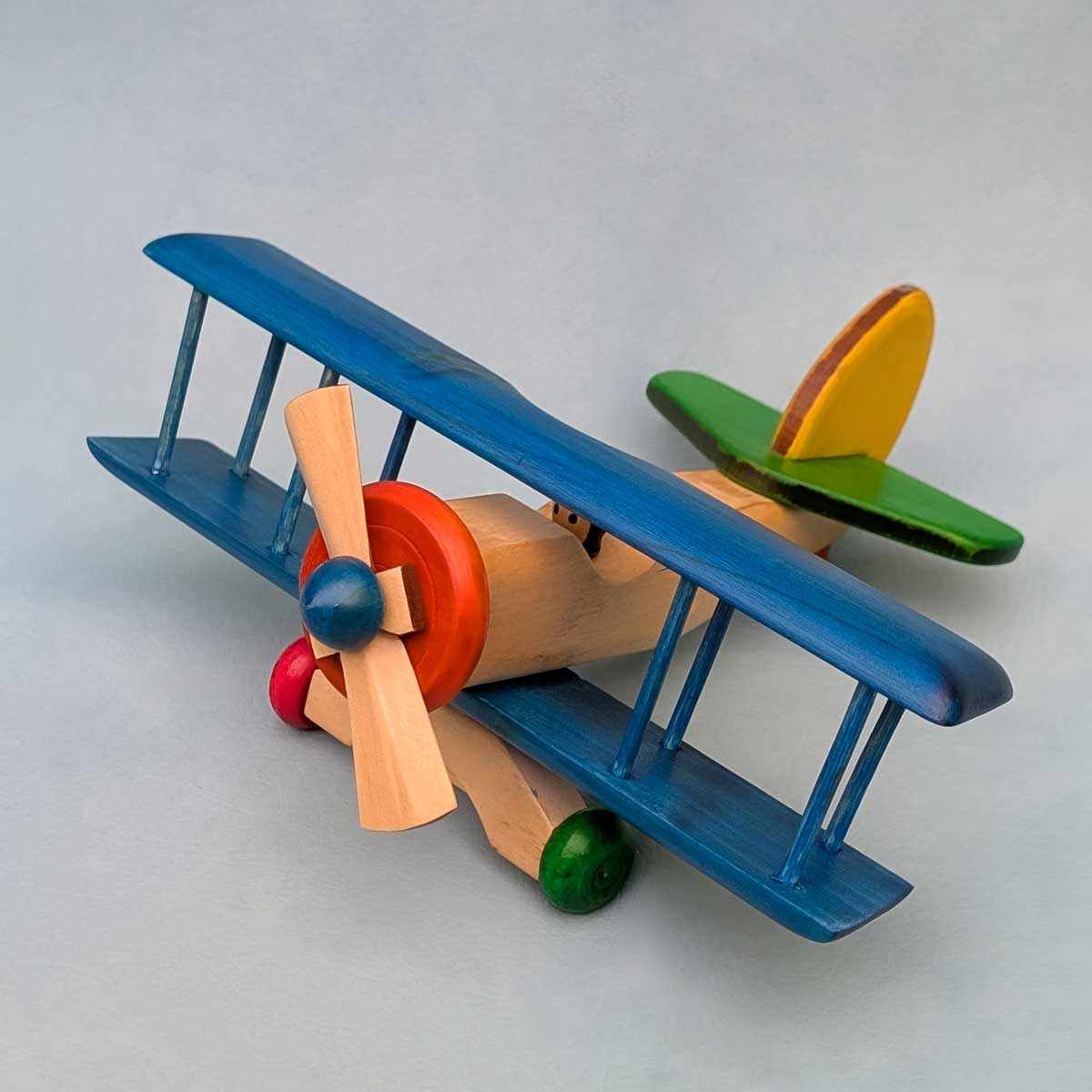 Avión biplano de madera multicolor, juguete artesanal para niños que estimula la imaginación. Color de alas azul