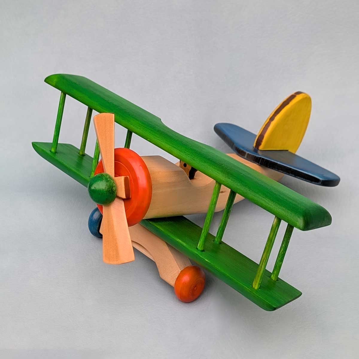 Avión biplano de madera multicolor, juguete artesanal para niños que estimula la imaginación. Color de alas verde