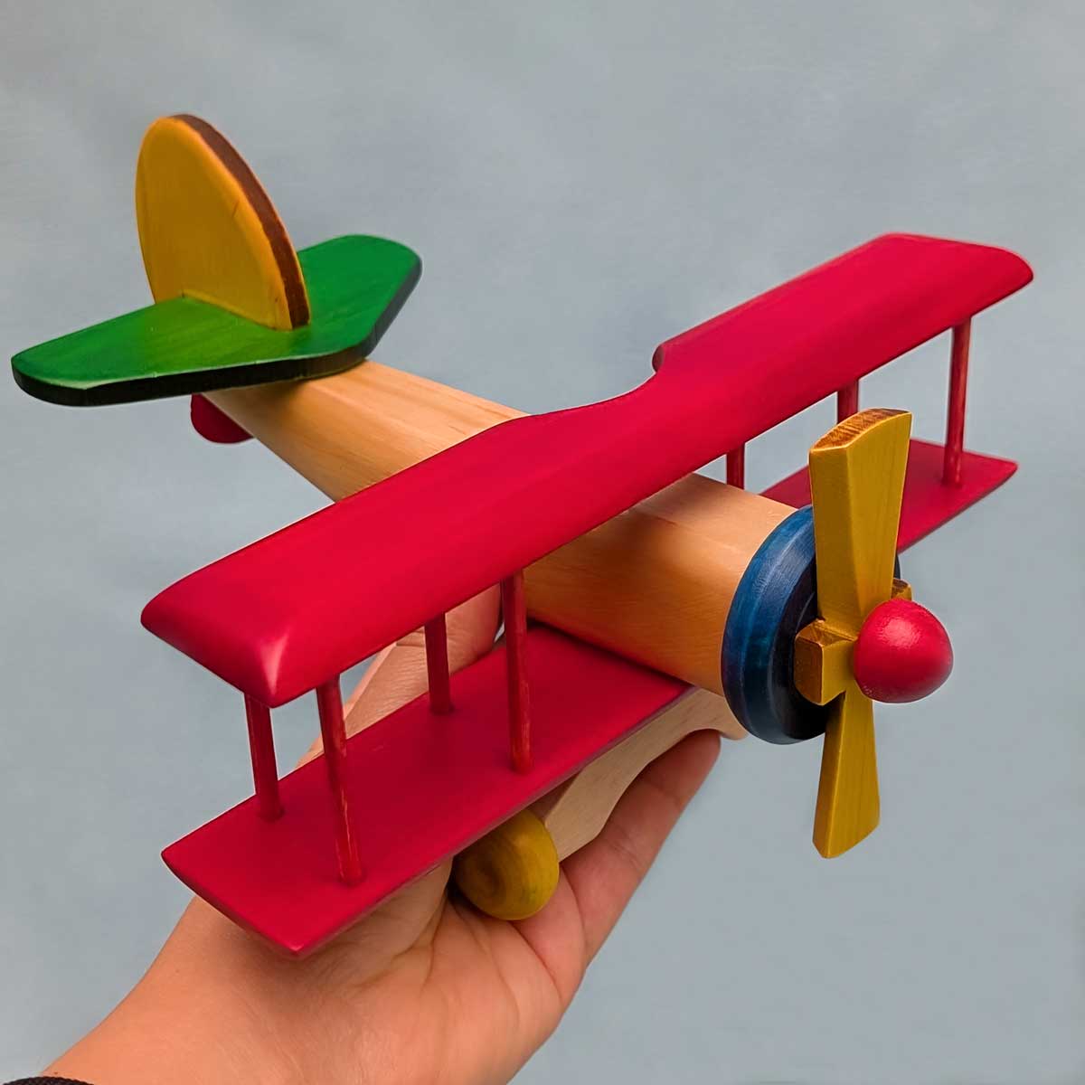 Avión biplano de madera multicolor, juguete artesanal para niños que estimula la imaginación. Referencia de tamaño con mano