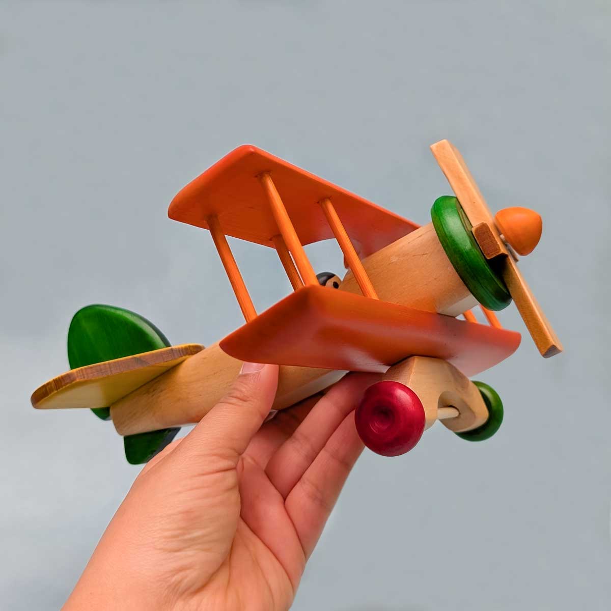 Avión biplano de madera multicolor, juguete artesanal para niños que estimula la imaginación. Referencia de tamaño en mano