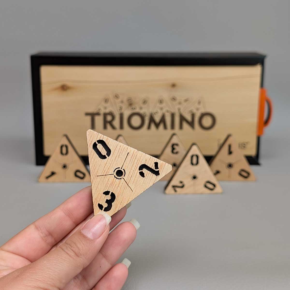 Juego de Tridominó en madera, perfecto para compartir en familia y ejercitar la mente. Foto detalle ficha y referencia de tamaño en mano