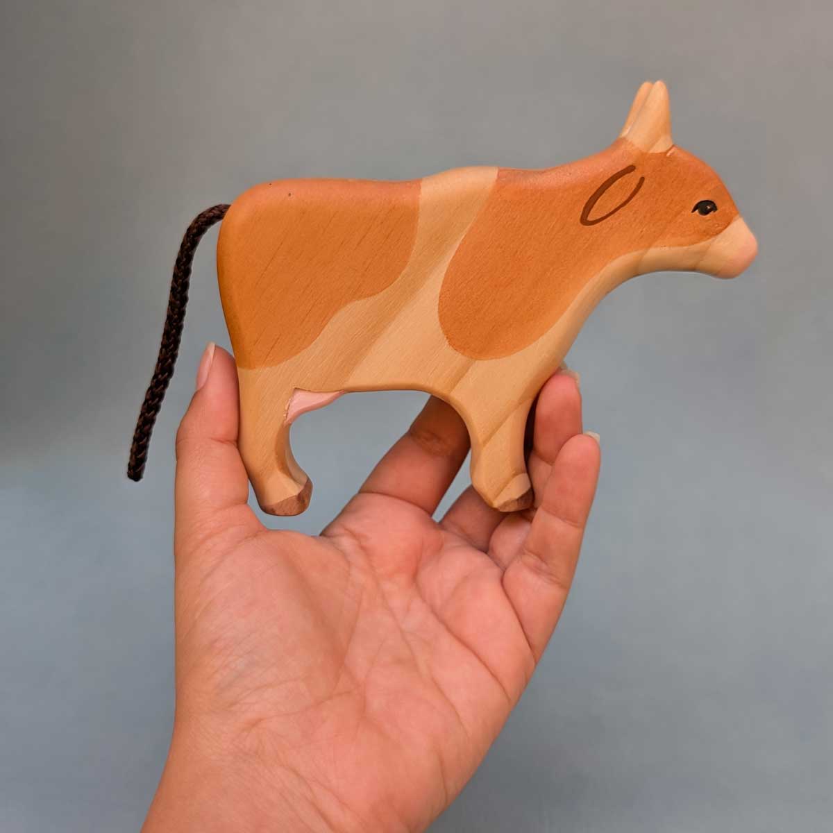 Vaca de madera, color de manchas miel,  juguete Montessori artesanal para estimular la imaginación infantil. Referencia de tamaño en mano